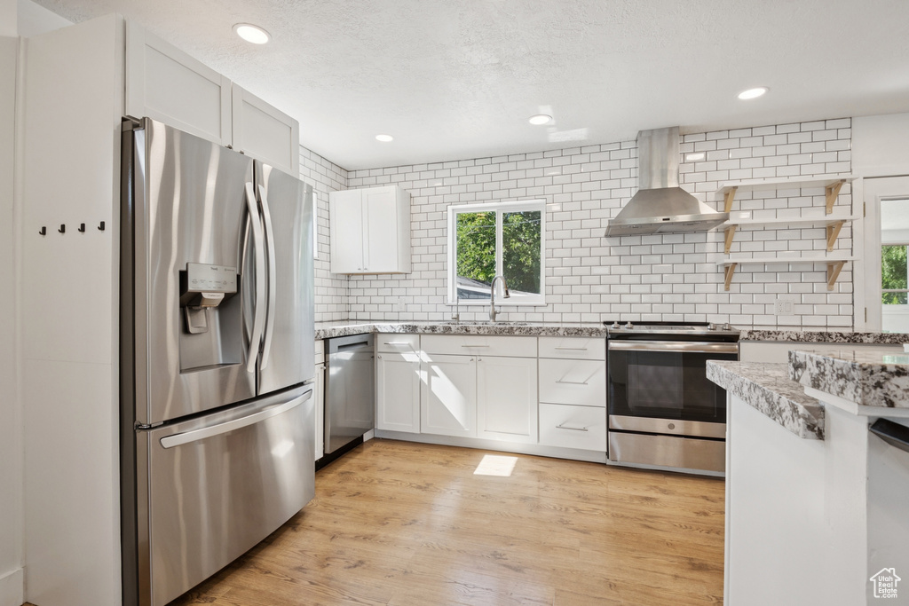Kitchen featuring appliances with stainless steel finishes, wall chimney exhaust hood, decorative backsplash, white cabinetry, and recessed lighting