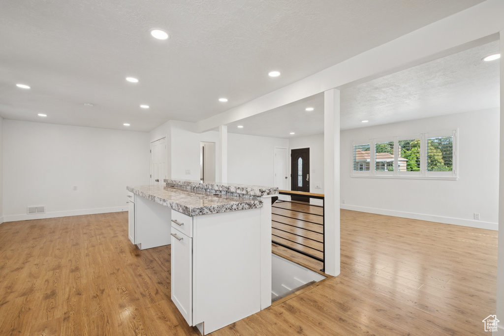 Kitchen featuring open floor plan, light wood-style flooring, a kitchen island, recessed lighting, and white cabinetry