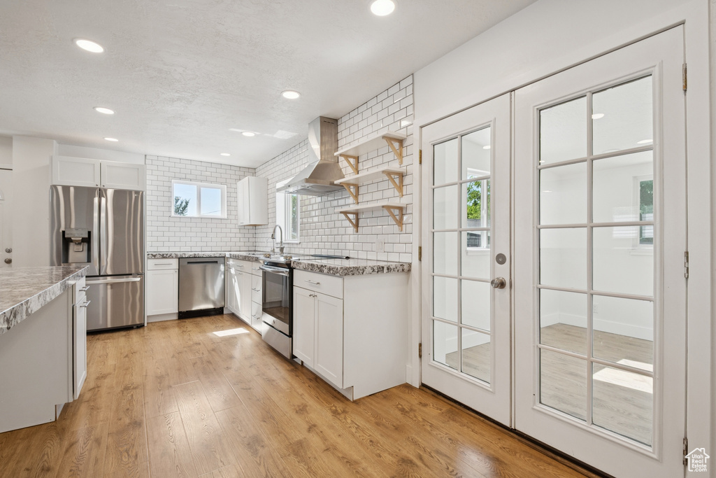 Kitchen with appliances with stainless steel finishes, ventilation hood, white cabinetry, tasteful backsplash, and light wood finished floors