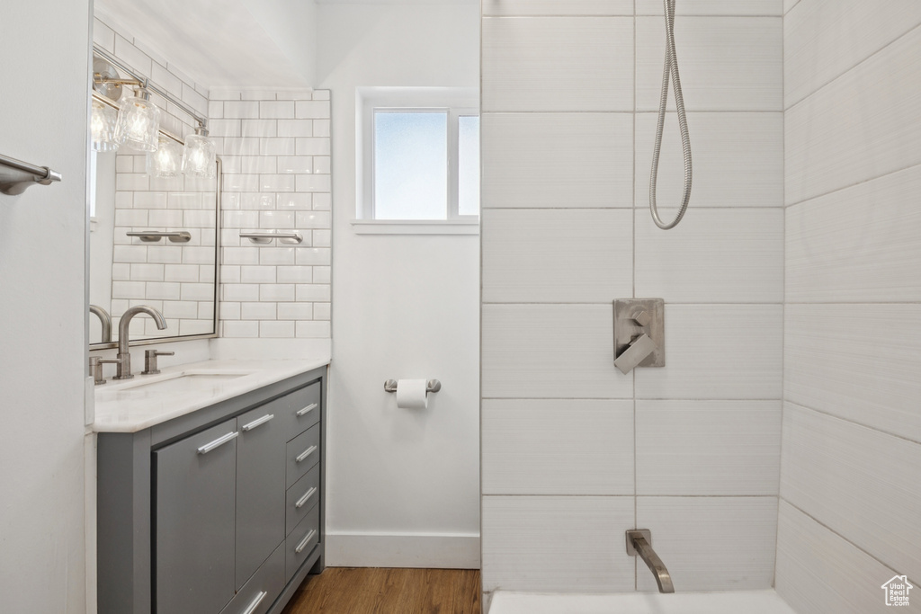 Full bath featuring vanity, tiled shower, and wood finished floors