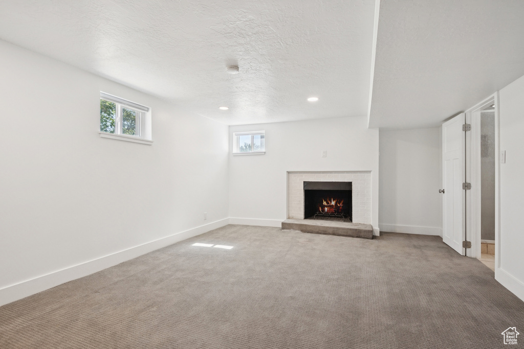 Unfurnished living room with a brick fireplace, carpet floors, a textured ceiling, and recessed lighting