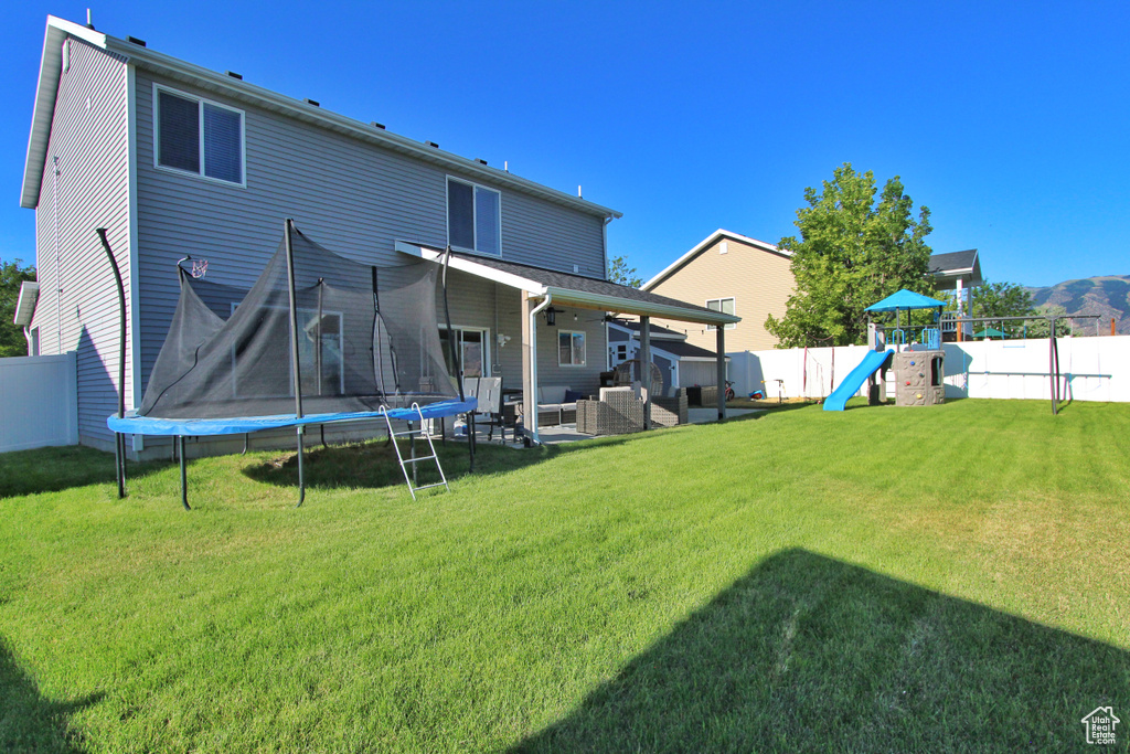Back of property with a trampoline, a fenced backyard, a playground, a ceiling fan, and a patio