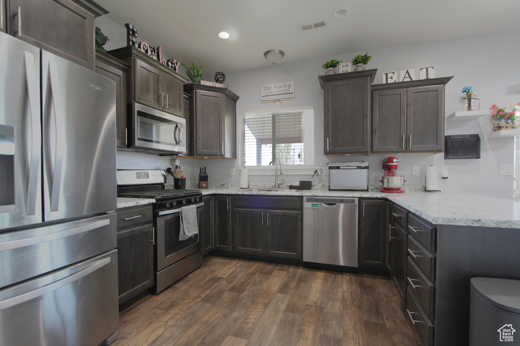 Kitchen with stainless steel appliances, light stone countertops, dark wood-style flooring, dark brown cabinetry, and recessed lighting