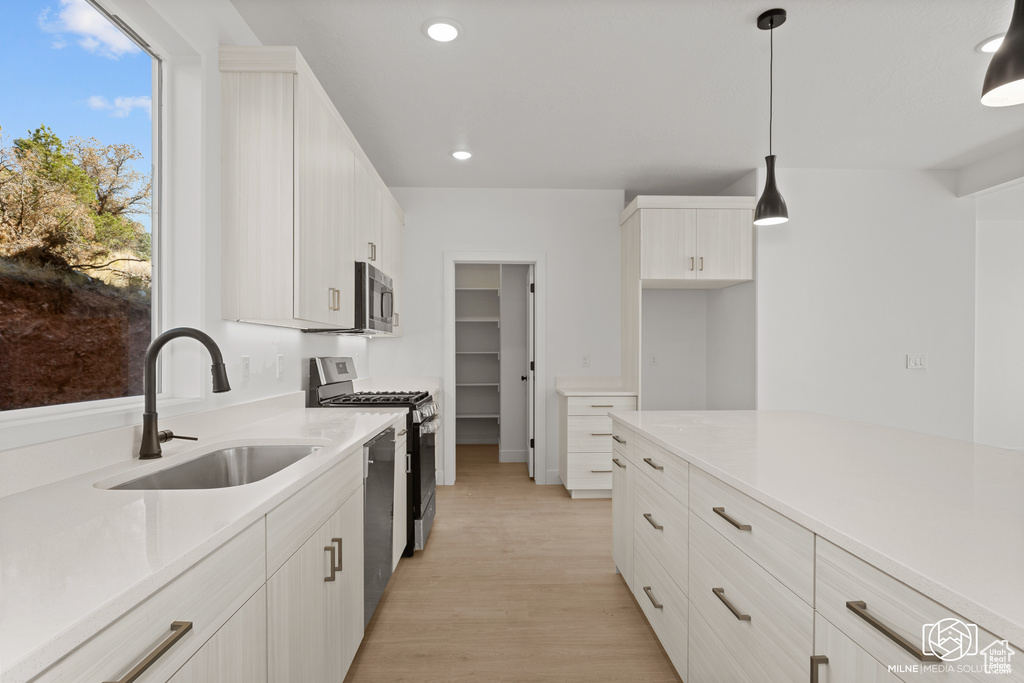 Kitchen with appliances with stainless steel finishes, light countertops, recessed lighting, light wood finished floors, and decorative light fixtures