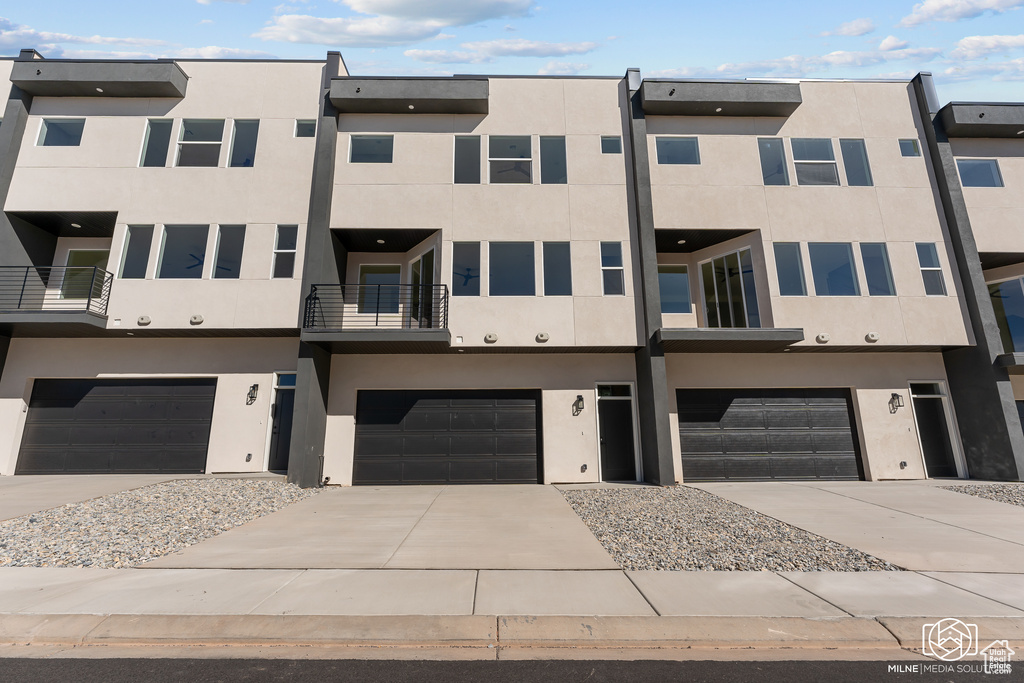 Back of house with a garage, stucco siding, driveway, and a balcony