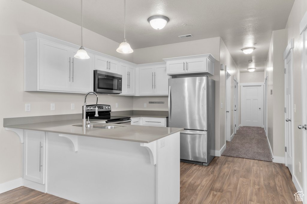 Kitchen with stainless steel appliances, a peninsula, wood finished floors, and white cabinetry