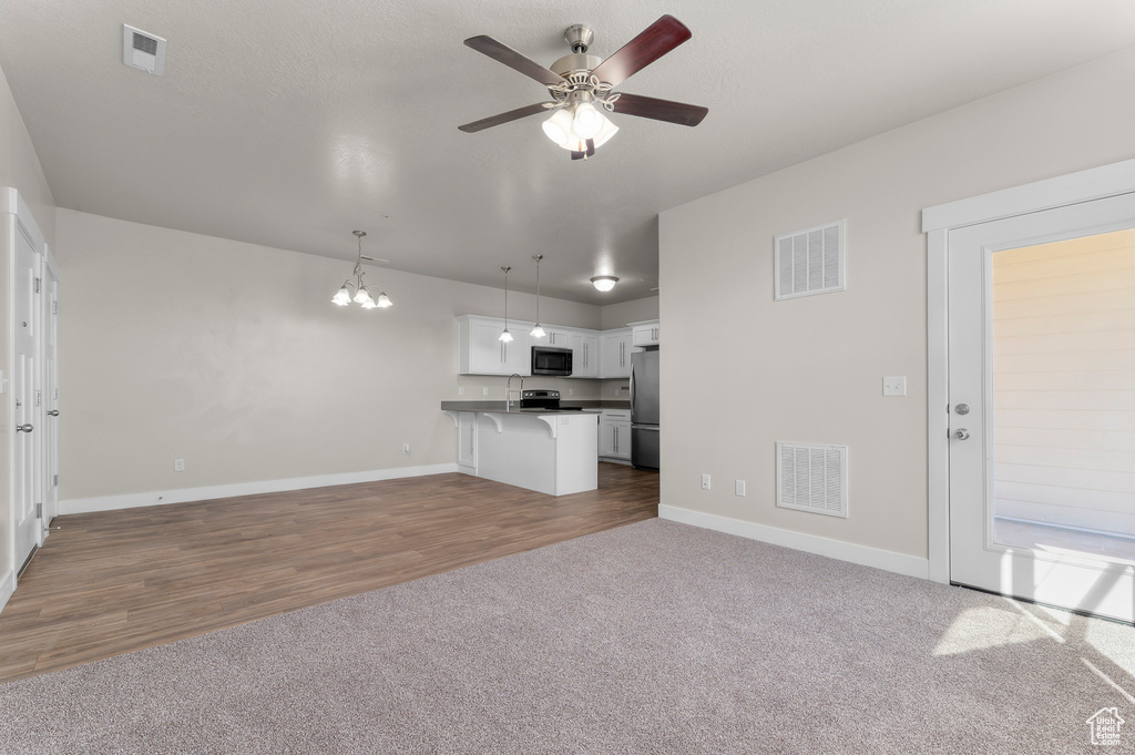 Unfurnished living room featuring a chandelier, a ceiling fan, carpet flooring, and wood finished floors