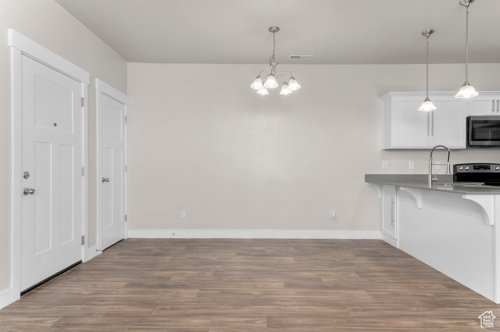 Kitchen with stainless steel appliances, a chandelier, a kitchen breakfast bar, wood finished floors, and white cabinets