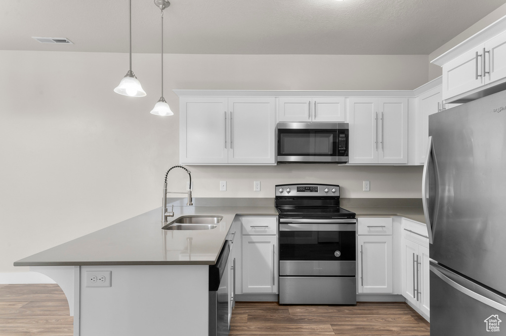 Kitchen with appliances with stainless steel finishes, a peninsula, and white cabinets