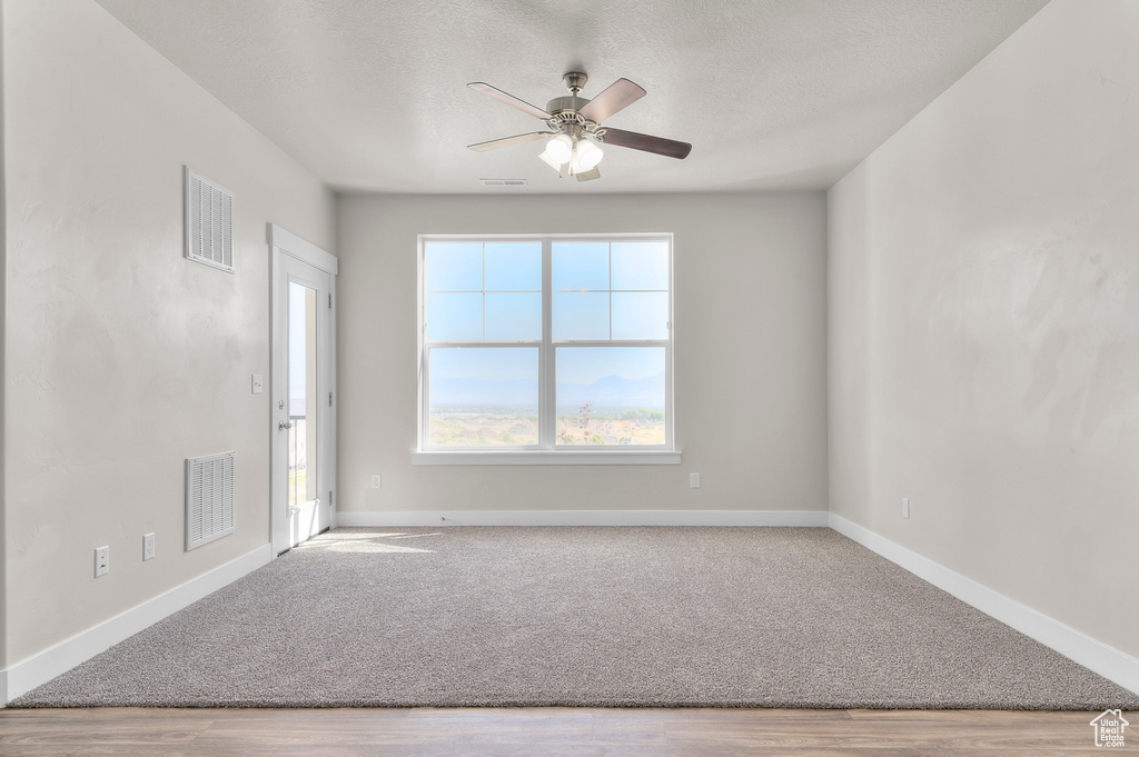 Carpeted empty room featuring wood finished floors, a ceiling fan, and a textured ceiling