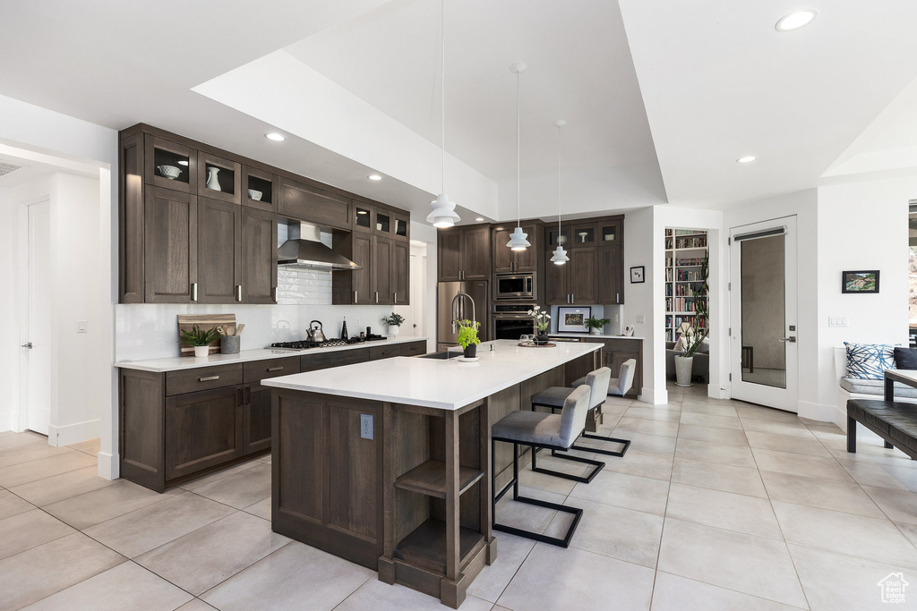 Kitchen featuring appliances with stainless steel finishes, wall chimney exhaust hood, light countertops, dark brown cabinetry, and light tile patterned floors