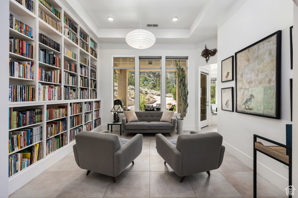 Sitting room featuring wall of books, a tray ceiling, and tile patterned flooring