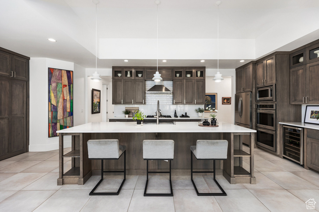 Kitchen featuring beverage cooler, appliances with stainless steel finishes, light countertops, a breakfast bar, and recessed lighting