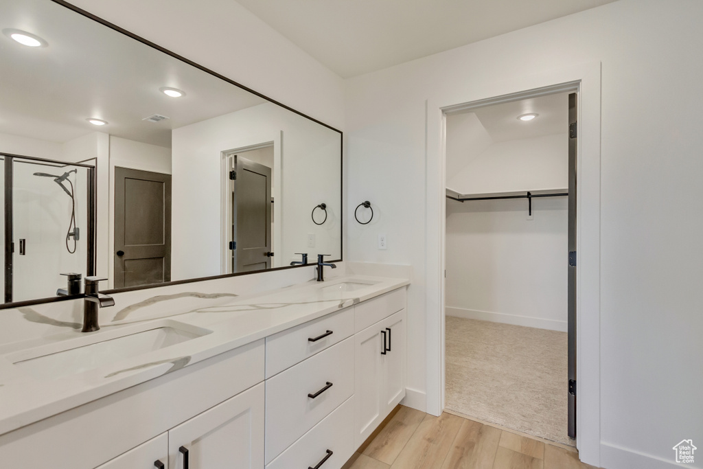 Bathroom with double vanity, wood finished floors, a walk in closet, a shower with shower door, and recessed lighting