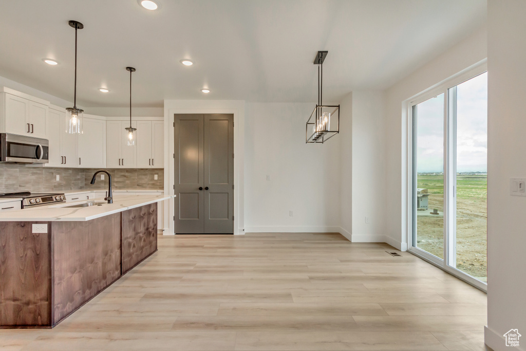 Kitchen featuring stainless steel appliances, tasteful backsplash, light wood-type flooring, white cabinetry, and recessed lighting