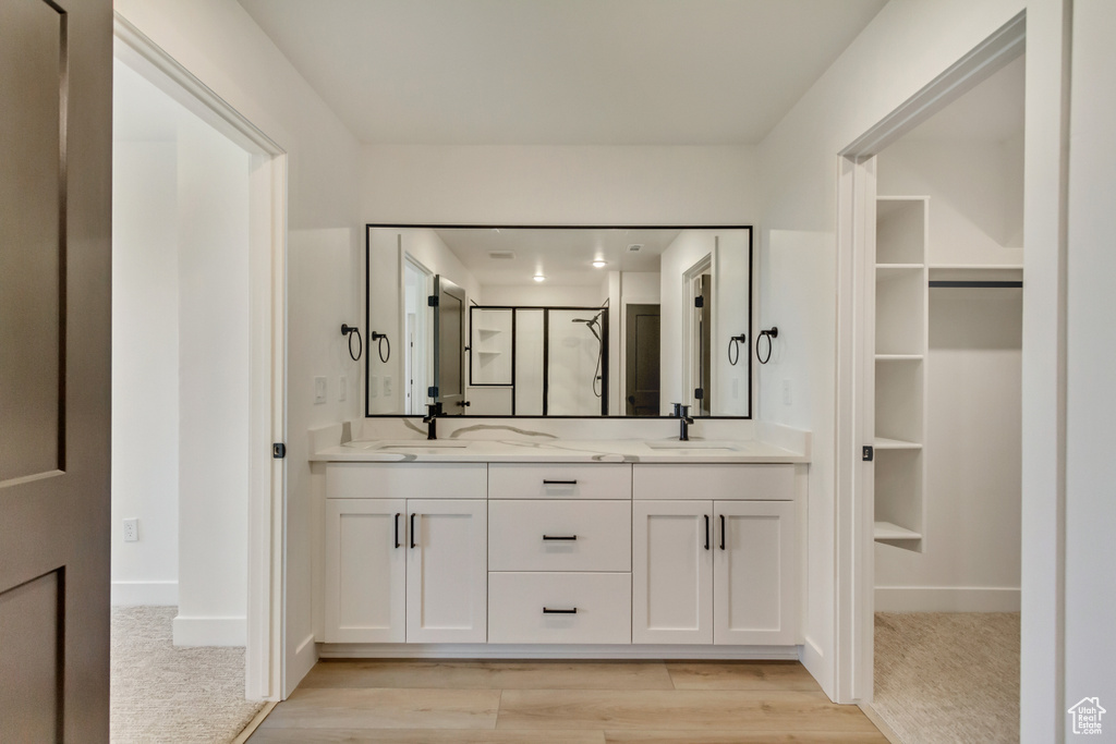 Full bath featuring double vanity, a shower stall, wood finished floors, and a spacious closet