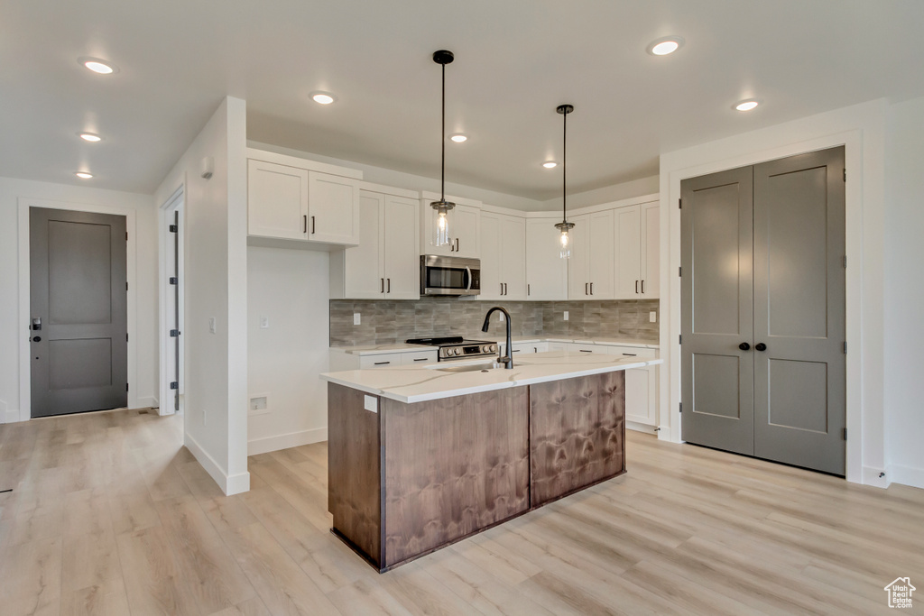 Kitchen featuring appliances with stainless steel finishes, light wood-style flooring, white cabinetry, backsplash, and recessed lighting