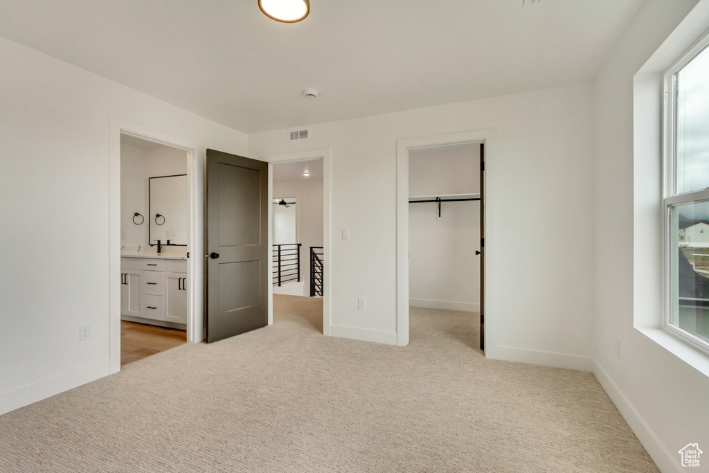 Unfurnished bedroom featuring light carpet, ensuite bathroom, and a spacious closet