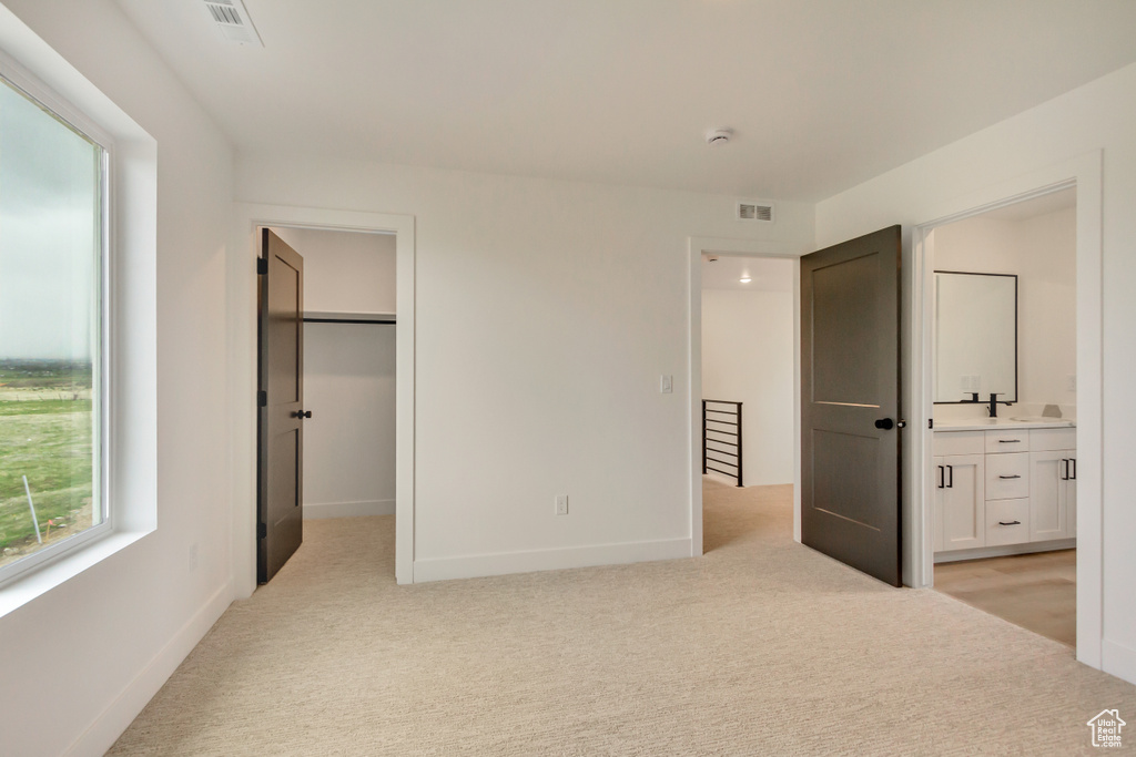 Unfurnished bedroom featuring light carpet, a walk in closet, and ensuite bathroom