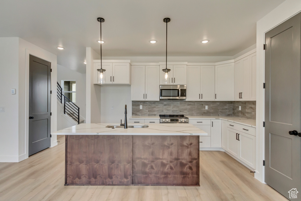 Kitchen with stainless steel appliances, light wood finished floors, decorative backsplash, white cabinetry, and recessed lighting