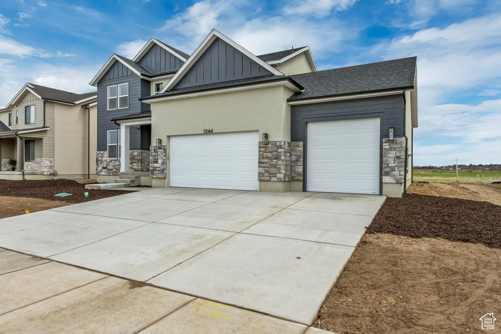 Craftsman inspired home with board and batten siding, stone siding, an attached garage, concrete driveway, and a shingled roof