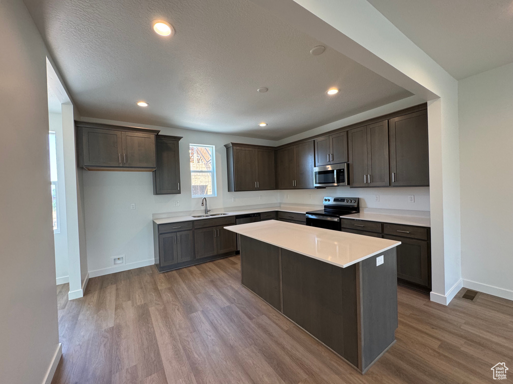 Kitchen with stainless steel appliances, dark brown cabinets, wood finished floors, light countertops, and recessed lighting