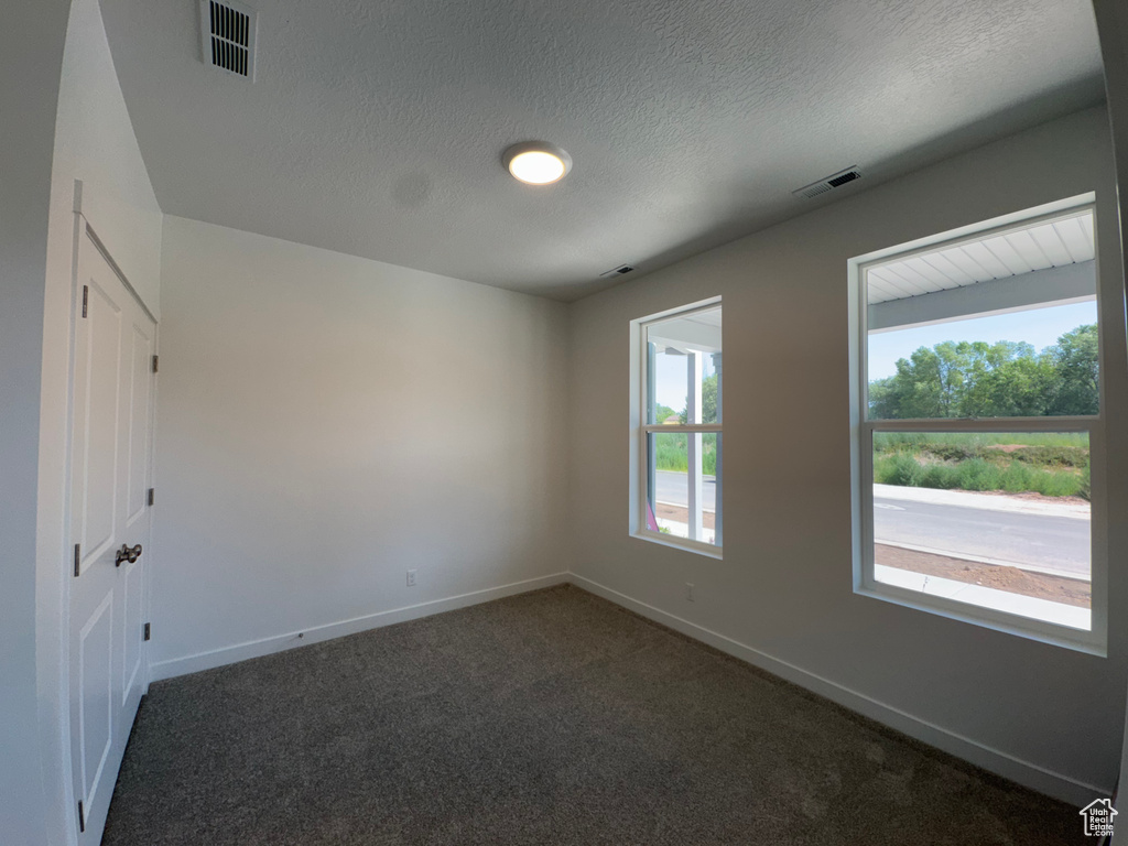Spare room featuring dark colored carpet and a textured ceiling
