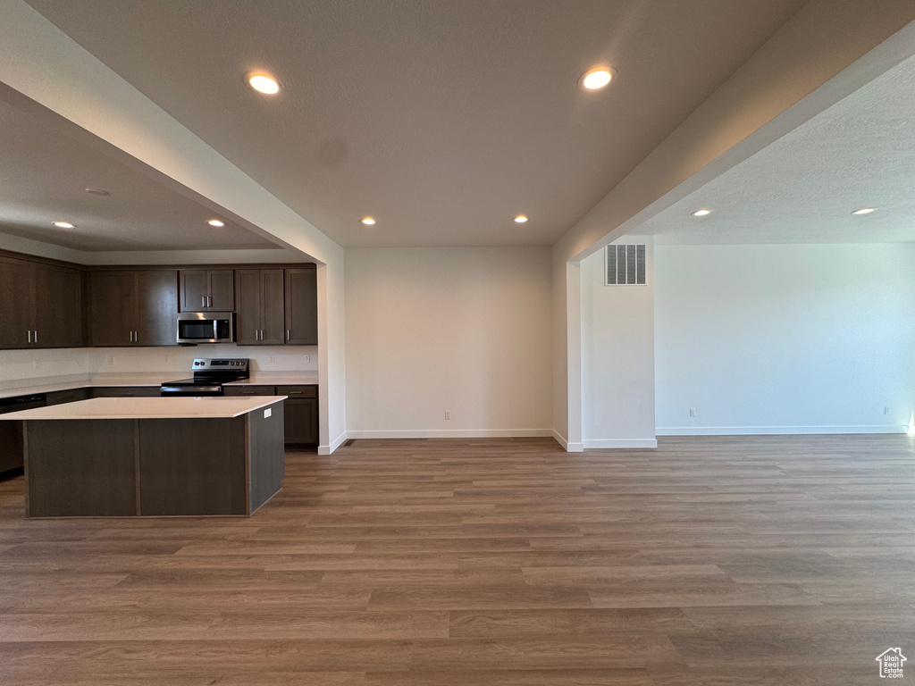 Kitchen featuring electric range oven, stainless steel microwave, open floor plan, recessed lighting, and dark brown cabinetry