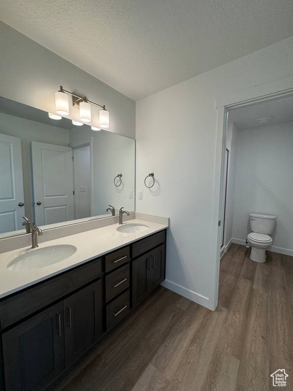 Full bath with wood finished floors, double vanity, and a textured ceiling