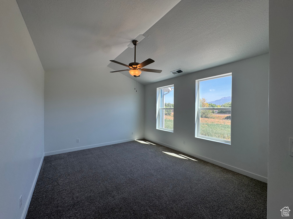 Empty room with ceiling fan, dark colored carpet, lofted ceiling, and a textured ceiling