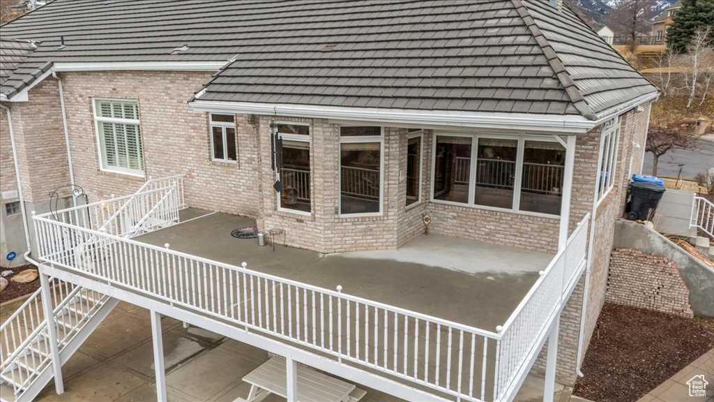 Back of house featuring brick siding, a tile roof, stairway, and a patio