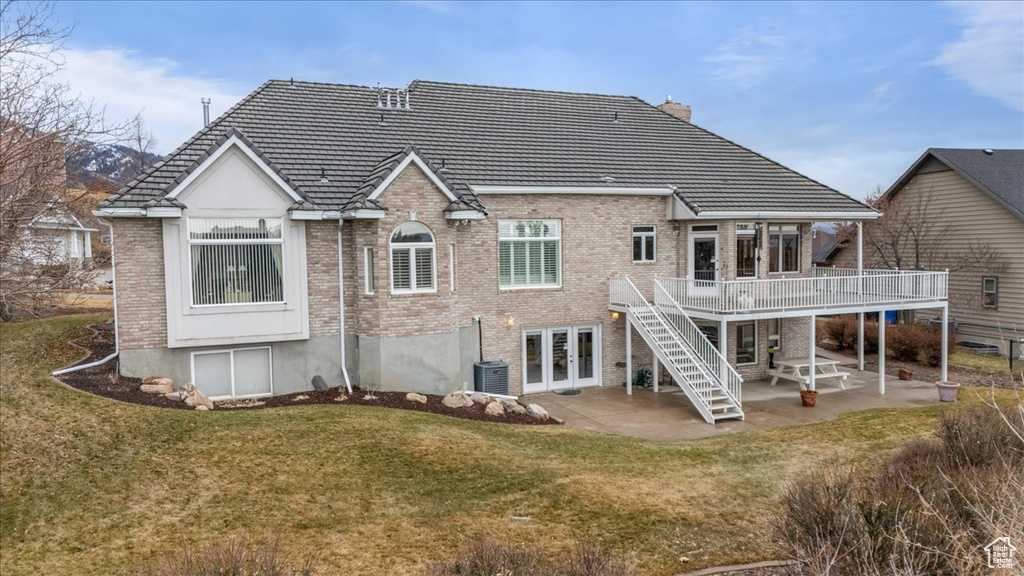 Back of house with french doors, a wooden deck, brick siding, and a patio