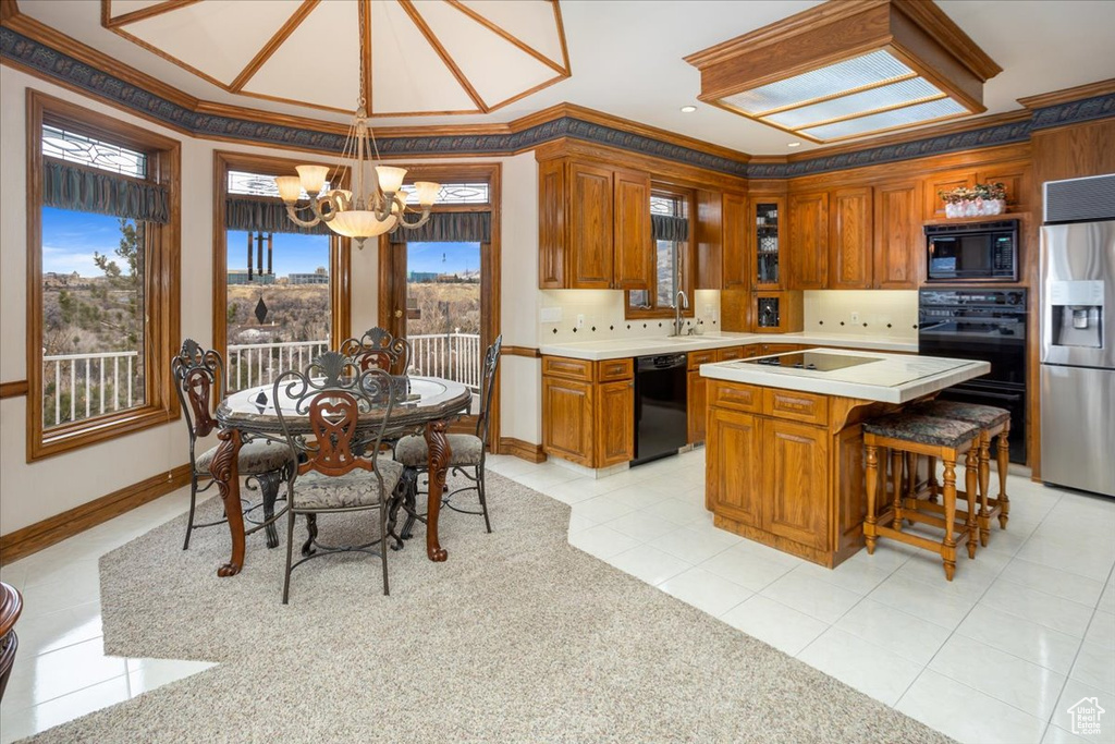 Kitchen featuring black appliances, a chandelier, light countertops, brown cabinets, and ornamental molding
