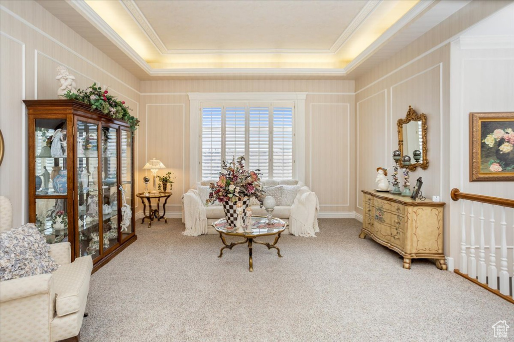 Living area featuring crown molding, carpet flooring, a raised ceiling, and a decorative wall