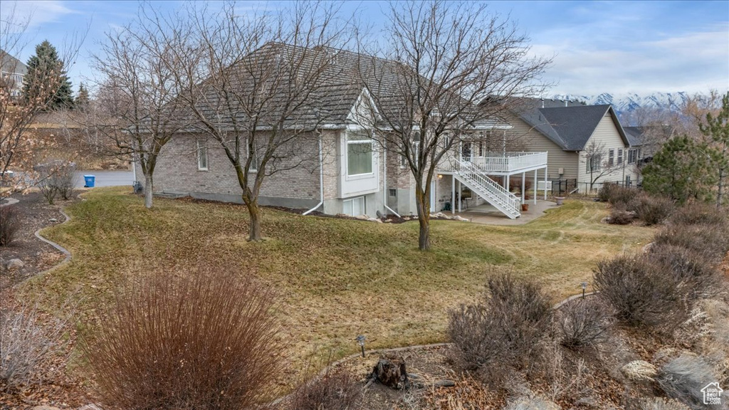 Rear view of house featuring stairway, brick siding, a wooden deck, and a lawn