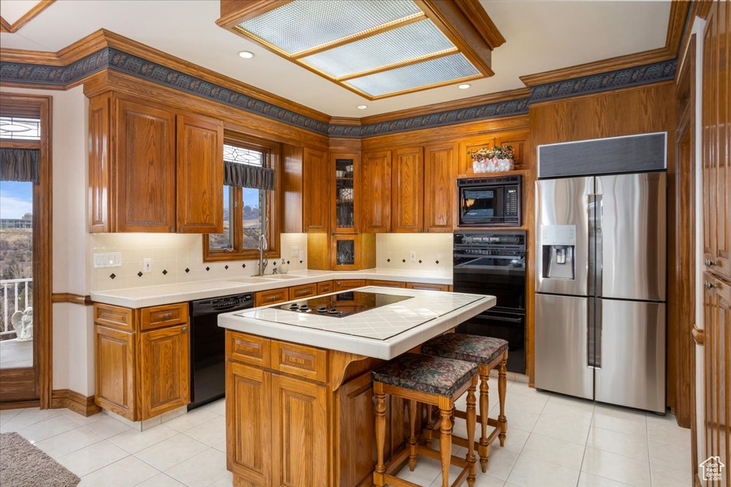 Kitchen featuring black appliances, ornamental molding, tile countertops, brown cabinets, and a center island