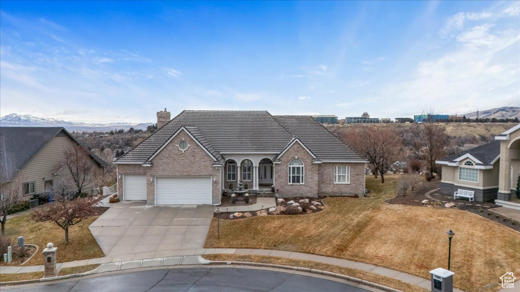 View of front of house with driveway, an attached garage, a tile roof, a chimney, and brick siding
