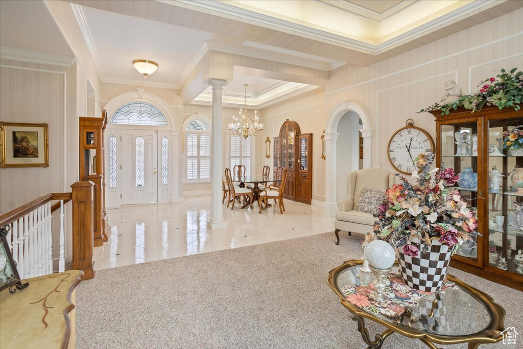 Foyer entrance featuring a chandelier, crown molding, ornate columns, tile patterned floors, and arched walkways