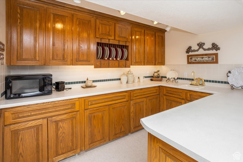 Kitchen featuring black microwave, tasteful backsplash, light countertops, and brown cabinets