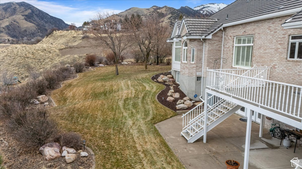 View of green lawn with a patio area, a deck with mountain view, and stairway