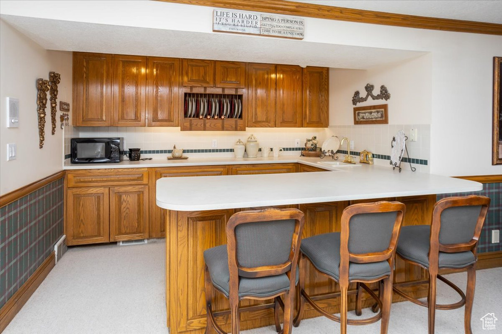 Kitchen featuring black microwave, light countertops, a peninsula, a kitchen bar, and brown cabinetry