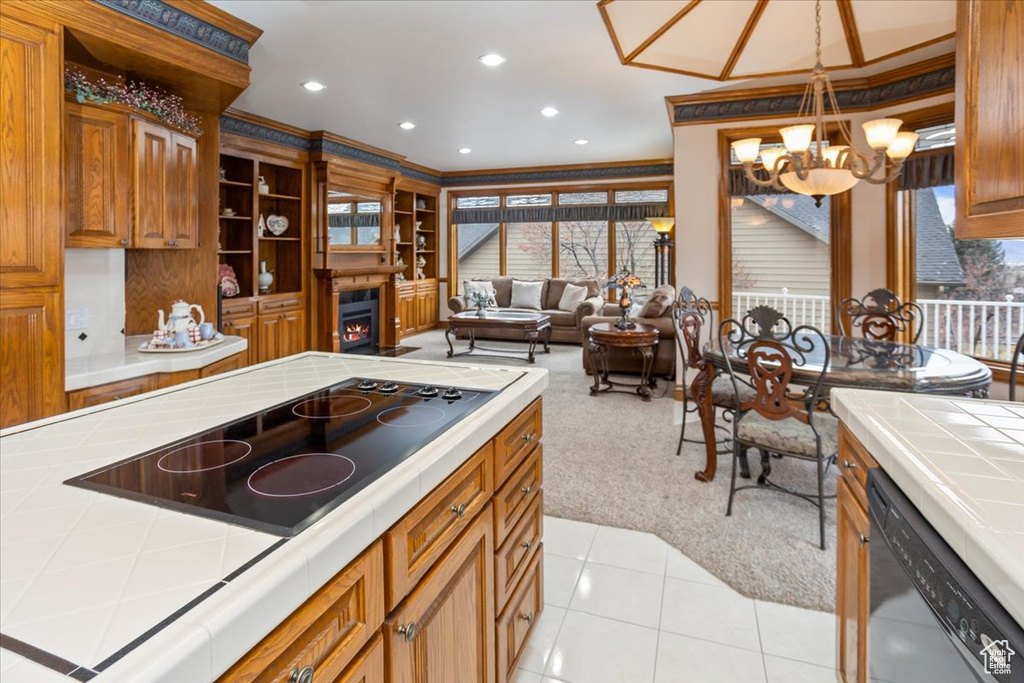 Kitchen with tile counters, black electric cooktop, dishwashing machine, a chandelier, and light carpet