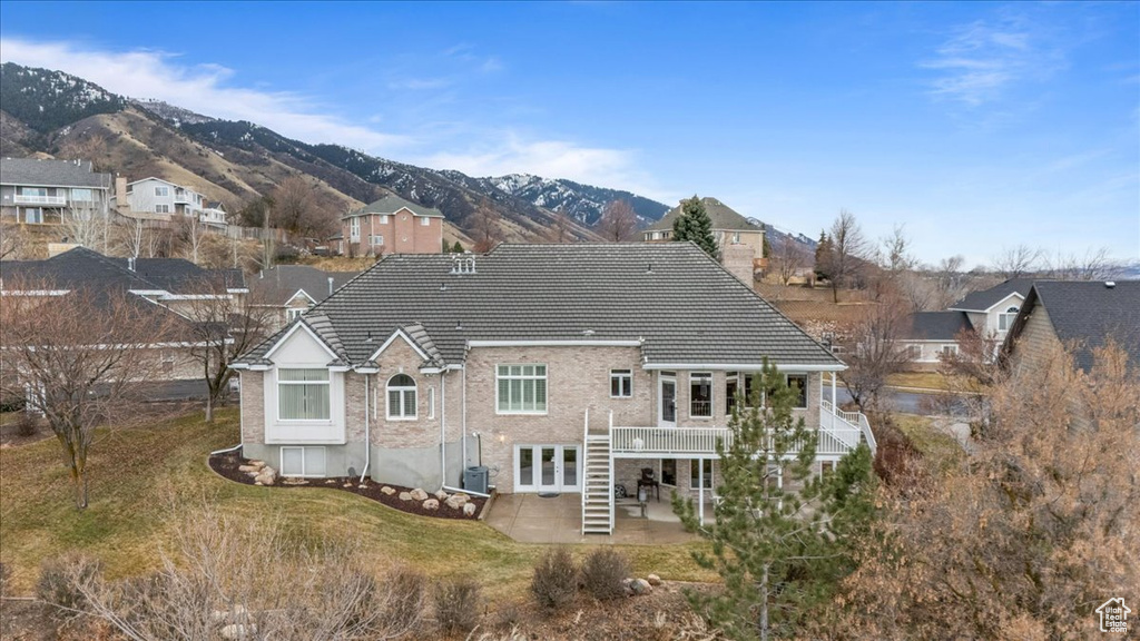 Back of property with a patio area, a deck with mountain view, a tiled roof, a residential view, and french doors