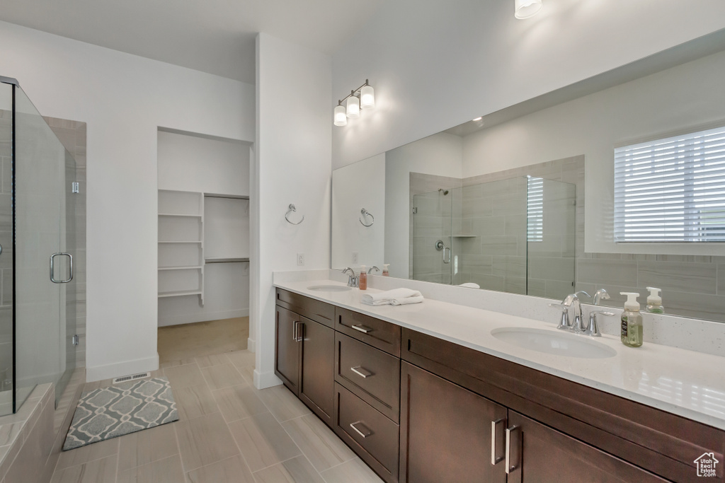 Bathroom featuring a shower stall, double vanity, a spacious closet, and tile patterned floors