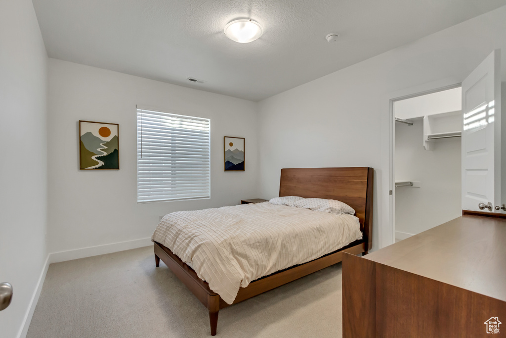 Bedroom with light colored carpet and a walk in closet