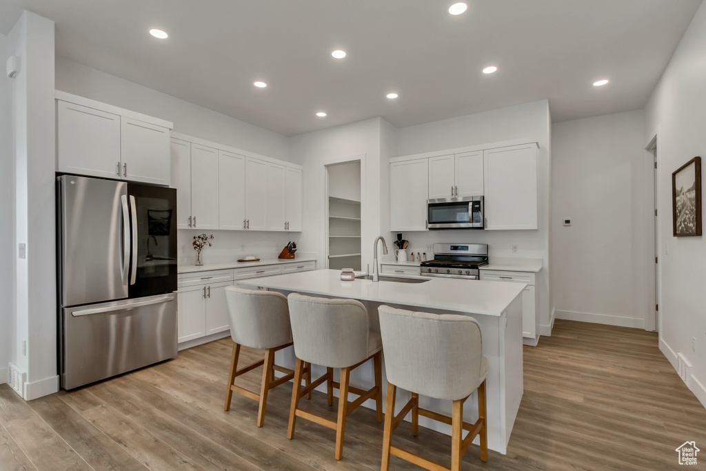 Kitchen featuring stainless steel appliances, light wood-type flooring, a center island with sink, light countertops, and recessed lighting