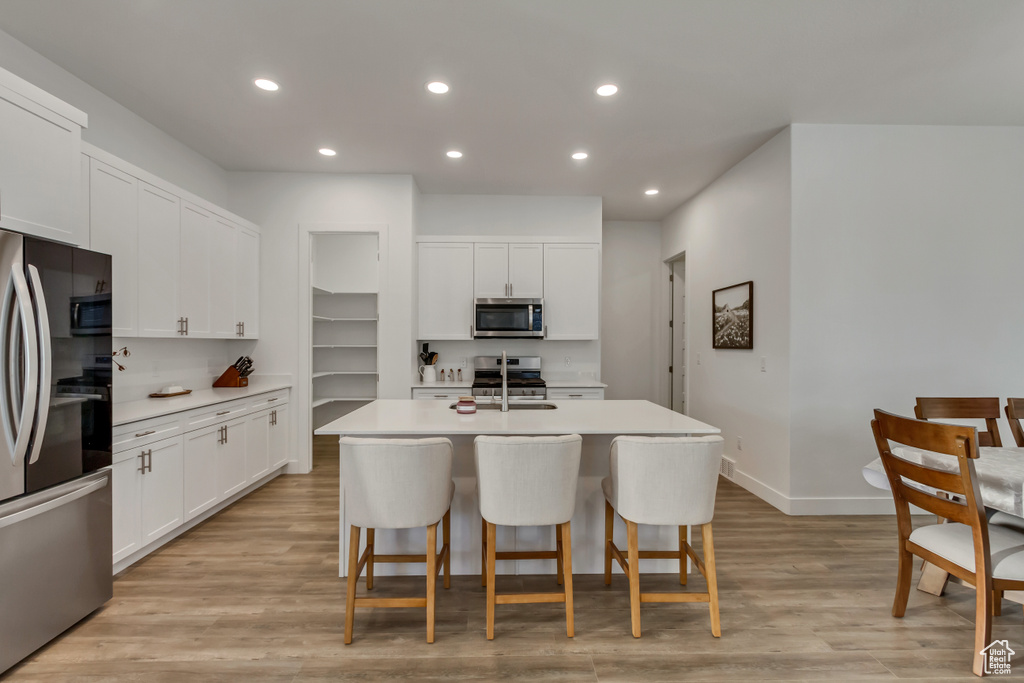 Kitchen with appliances with stainless steel finishes, a breakfast bar, recessed lighting, an island with sink, and white cabinetry