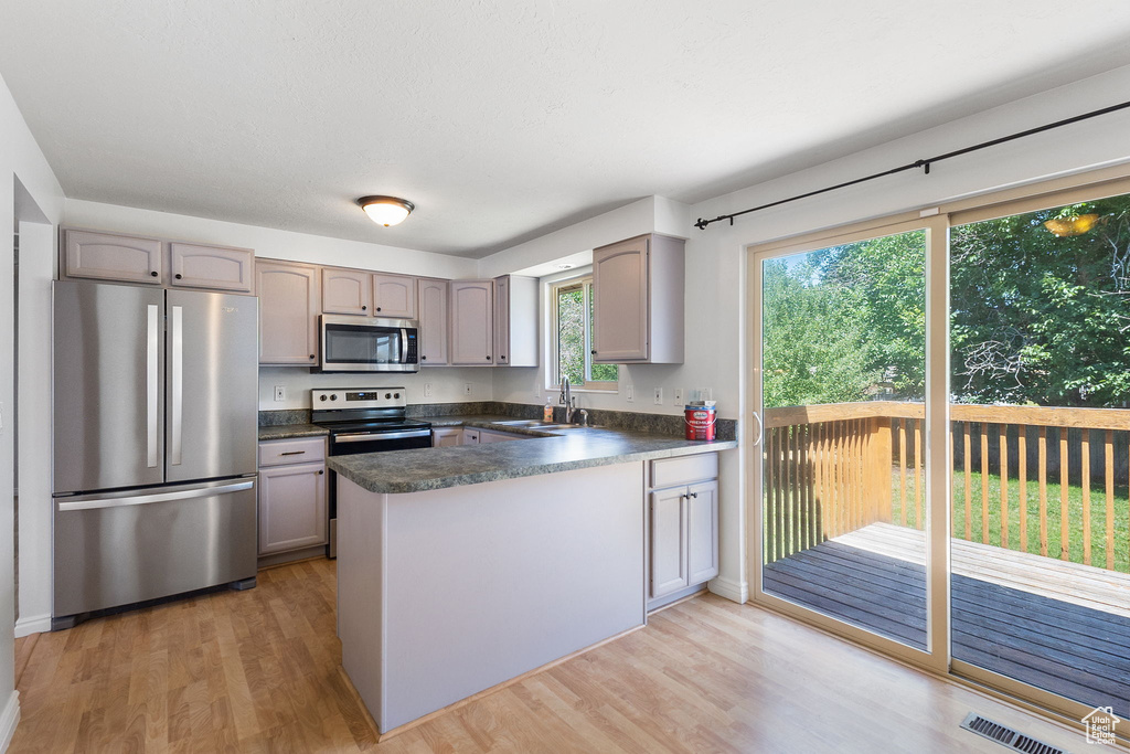 Kitchen with stainless steel appliances, dark countertops, a peninsula, light wood-style flooring, and gray cabinets