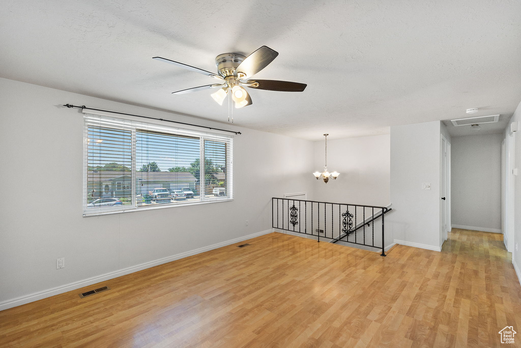 Empty room featuring light wood-style floors, a chandelier, and ceiling fan