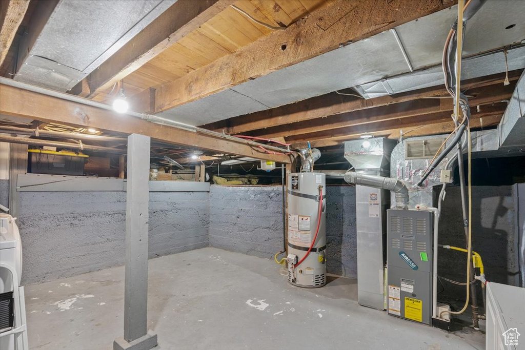 Unfinished below grade area featuring secured water heater, heating unit, and washer / dryer